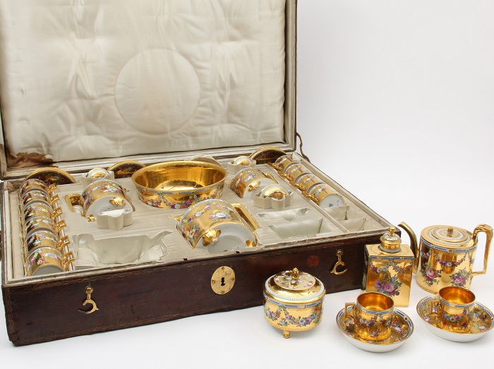 Golden chocolate service, featuring cups, saucers, and pouring vessels, inside a leather case