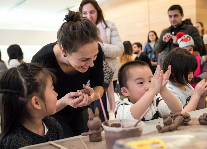 Children making shapes with clay while an instructor looks over their shoulder