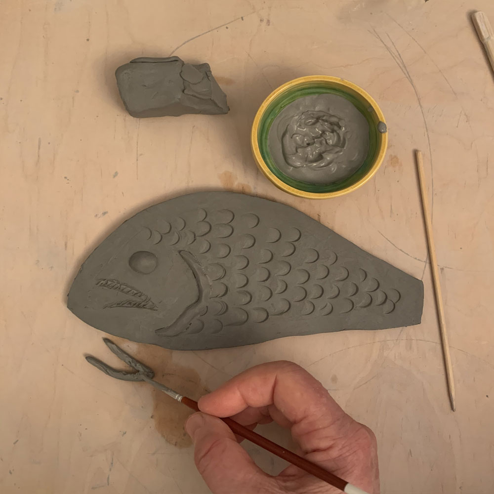 Brushing slip onto a clay fish