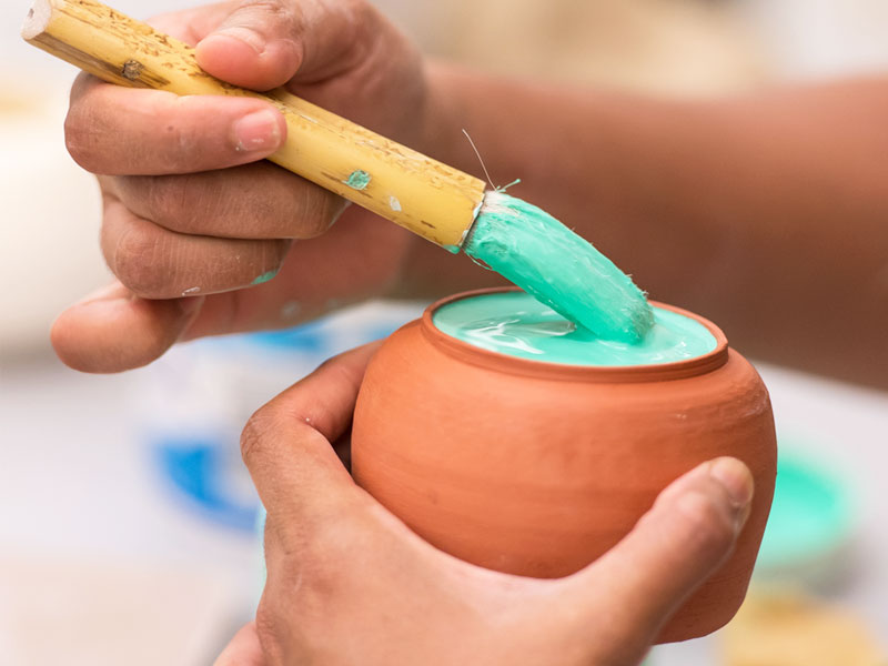 Hands of someone glazing a ceramic vessel with green glaze