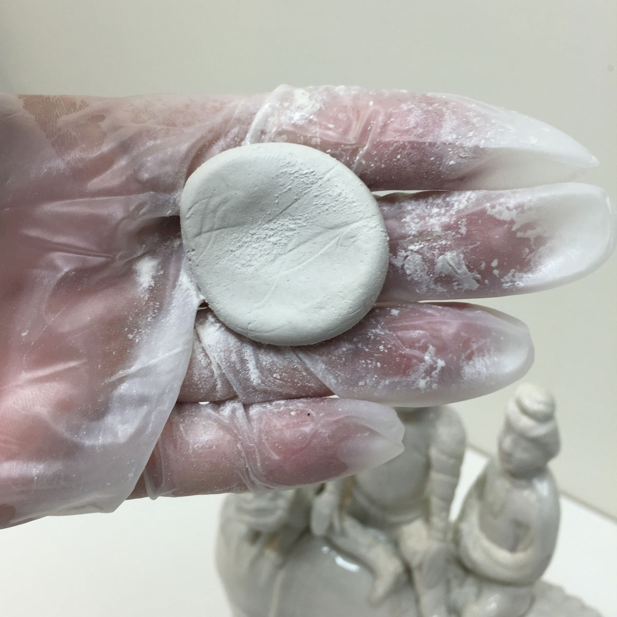 Gloved hand holding a small circle of clay