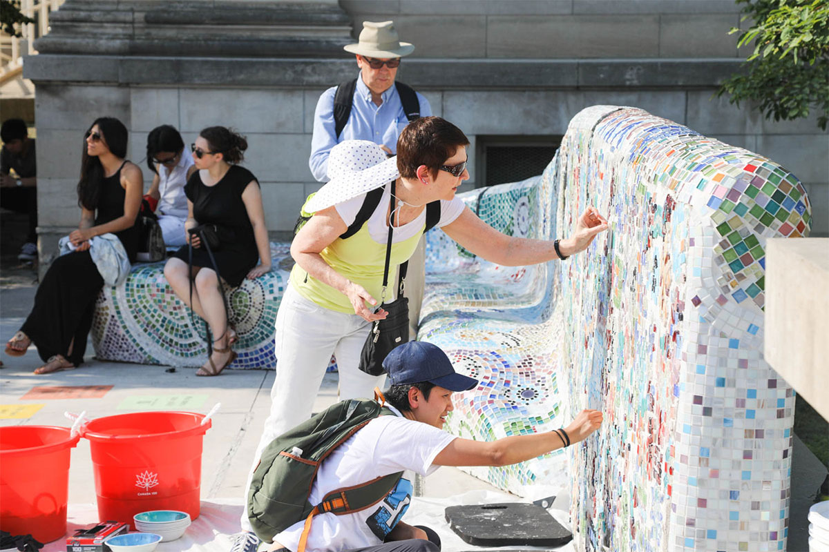 People outside tiling a mosaic wall