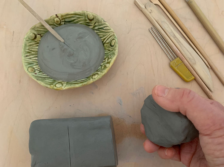 Clay and clay tools with a hand holding a ball of clay