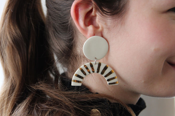 Woman wearing white ceramic earrings while a circular stud and dangling half moon with gold stripes