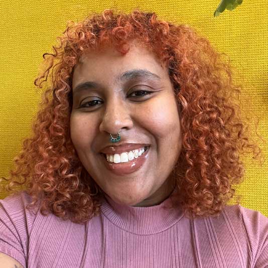 Curator Sarah Edo wearing a purple shirt on a yellow background