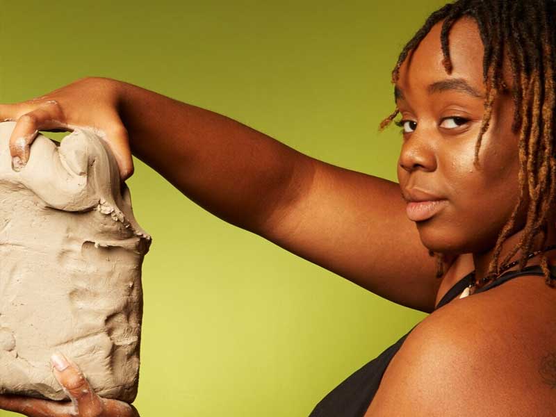 Shannon Weston holding a block of clay against a green background