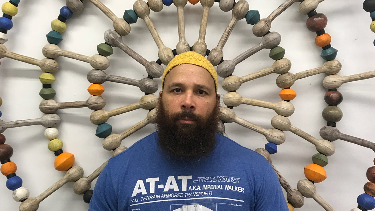 Artist Sharif Bey standing in front of a wheel of ceramic beads