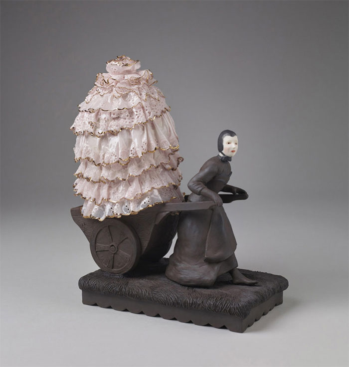 Porcelain figure pulling a wheelbarrow containing a lace dress