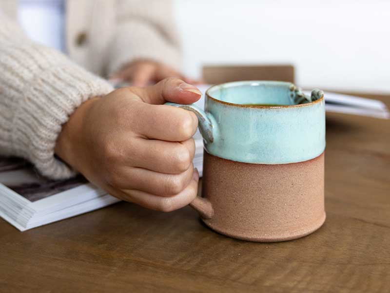 Shop-Thumbnail Hand holding a brown and turquoise ceramic mug