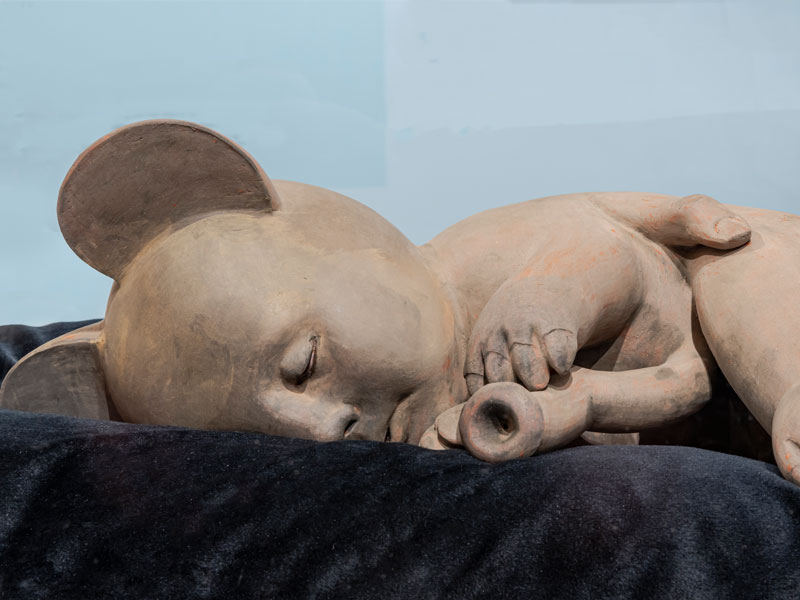 A close up of a ceramic figure in the form of a baby / animal hybrid