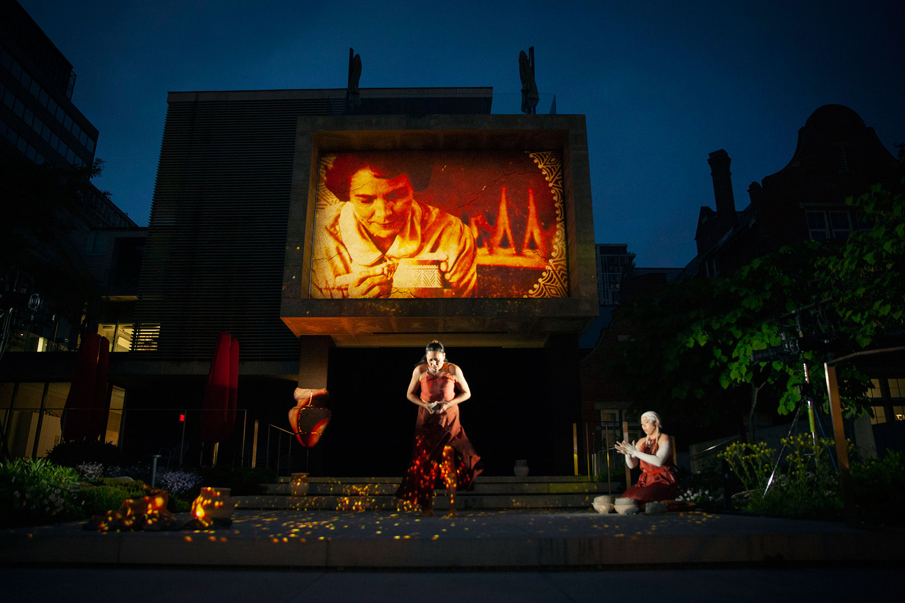 Two Indigenous women performing with a large video projection behind them